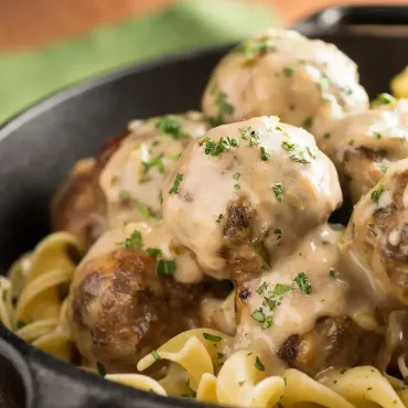 Creamy meatballs over egg noodles, garnished with chopped parsley in a black bowl