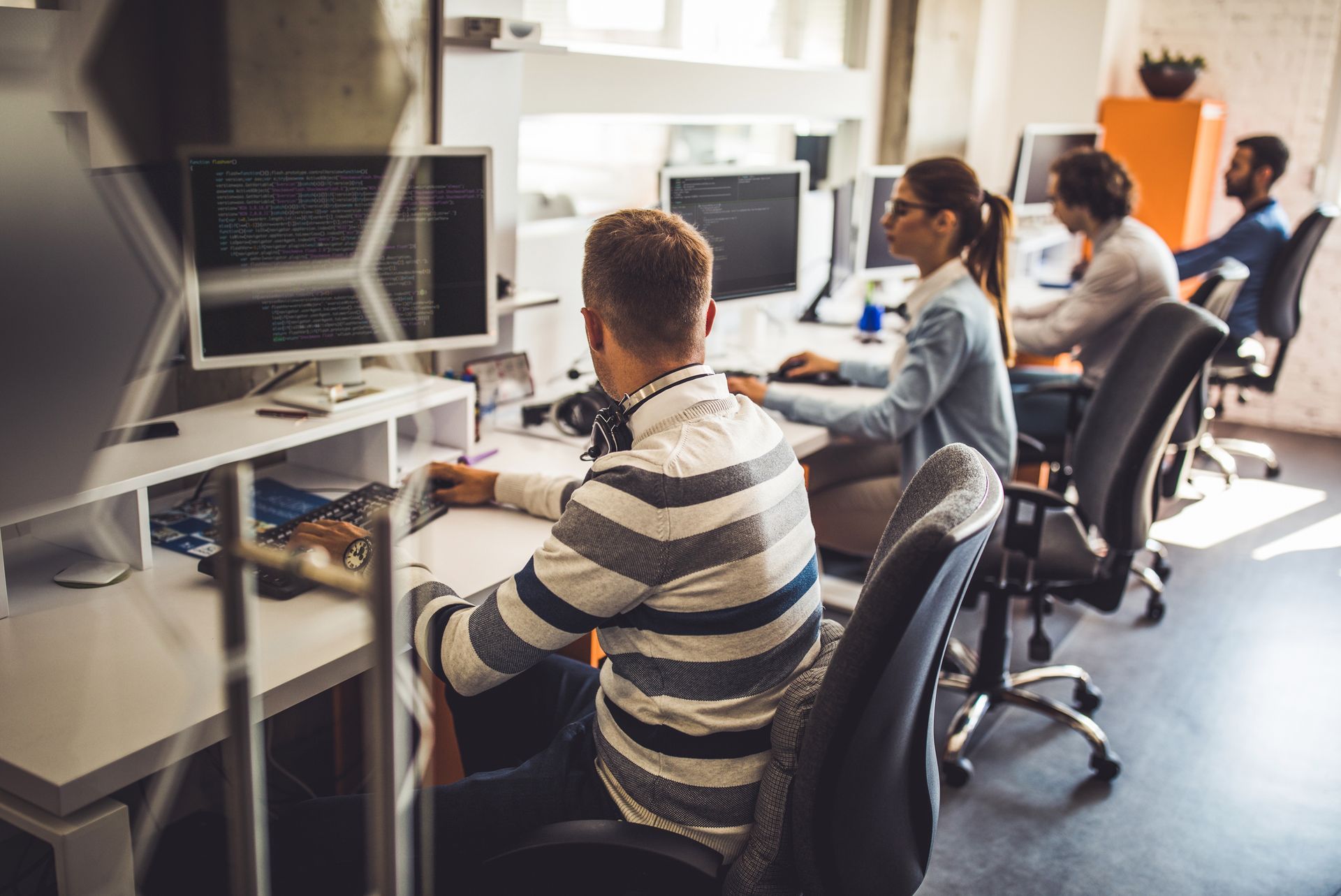 Un gruppo di persone è seduto alle scrivanie di un ufficio e lavora al computer.