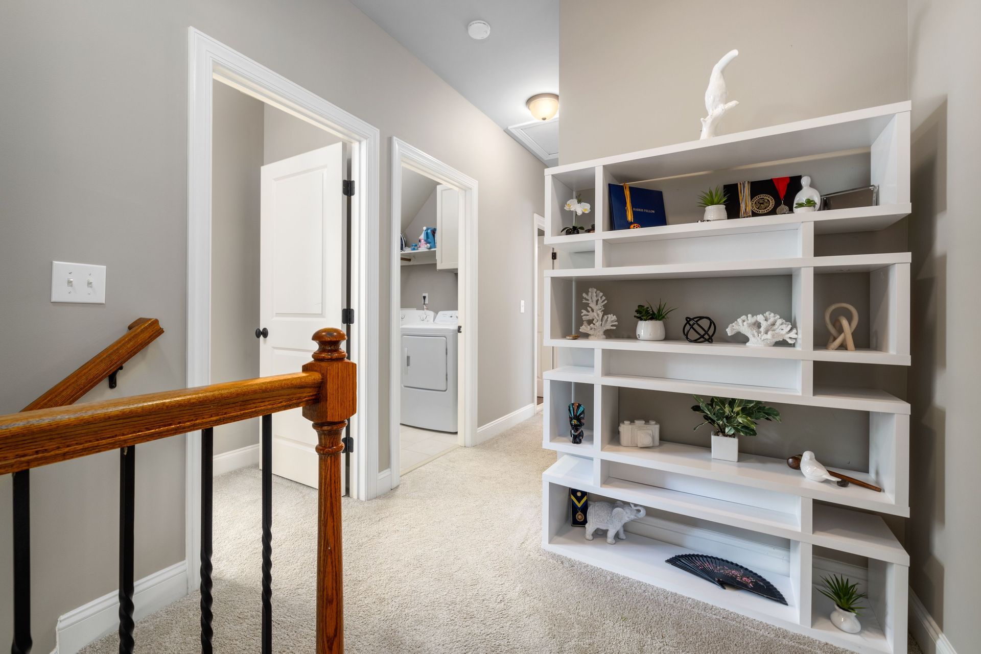 White hallway with open doors, built-in shelving, and a staircase railing in a bright home interior.