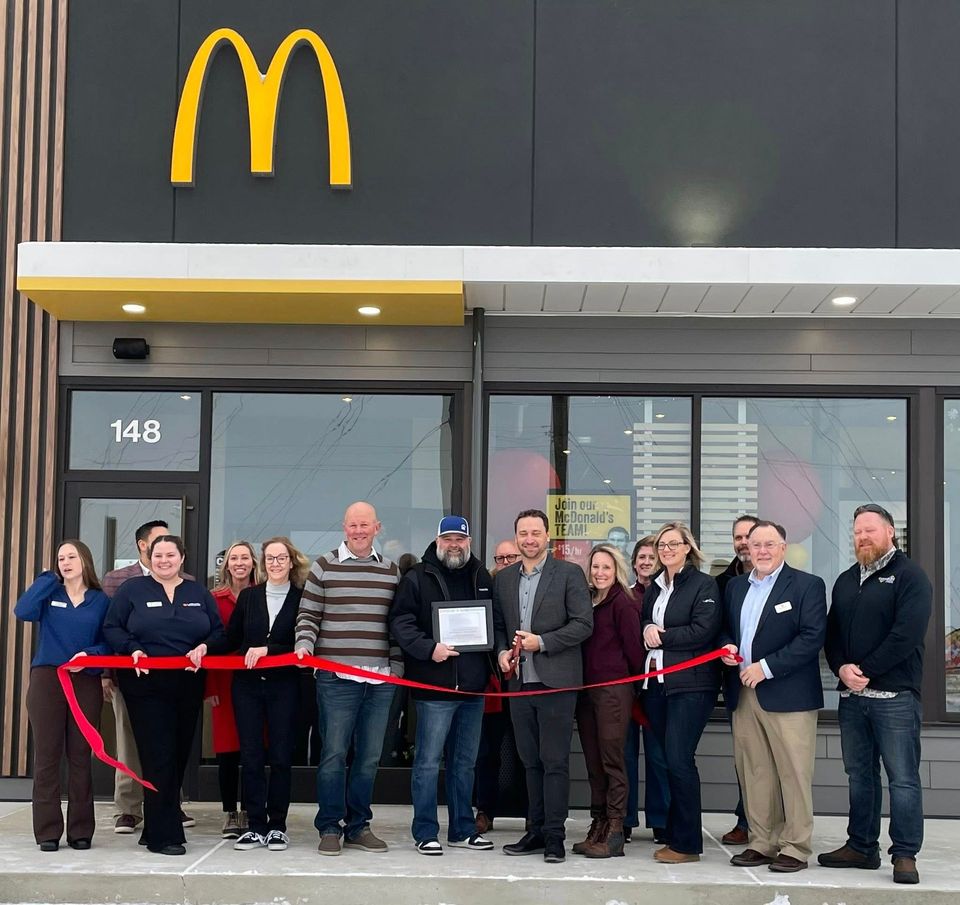 People cutting a red ribbon in front of a new McDonald's restaurant at location 148; they are celebrating the grand opening.
