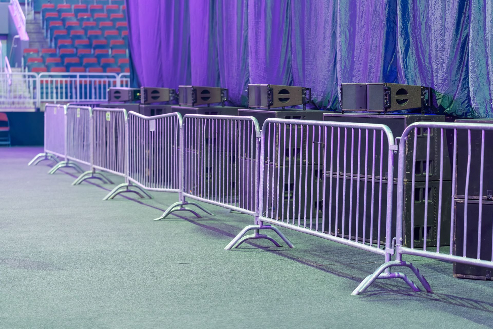 Metal crowd control barriers lined up in front of a stage with speakers and seating area.