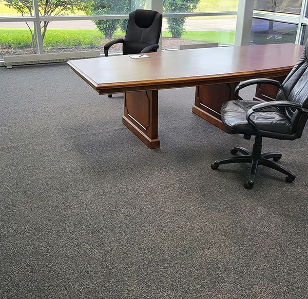 Office space with a large wooden desk, two black chairs, and gray carpet.