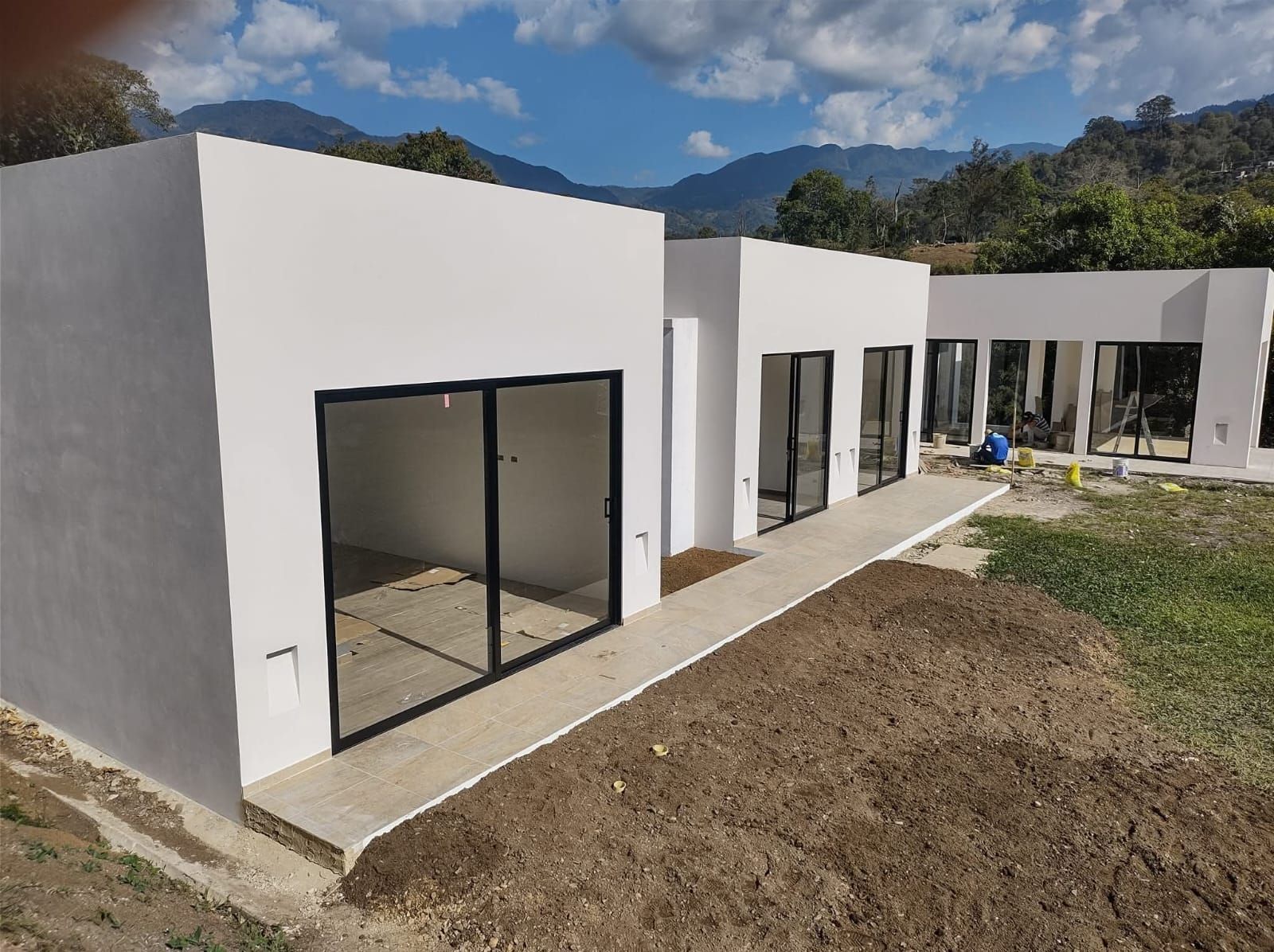 Exterior de una casa moderna de color blanco con grandes ventanales y un camino curvo en el patio bajo un cielo azul.