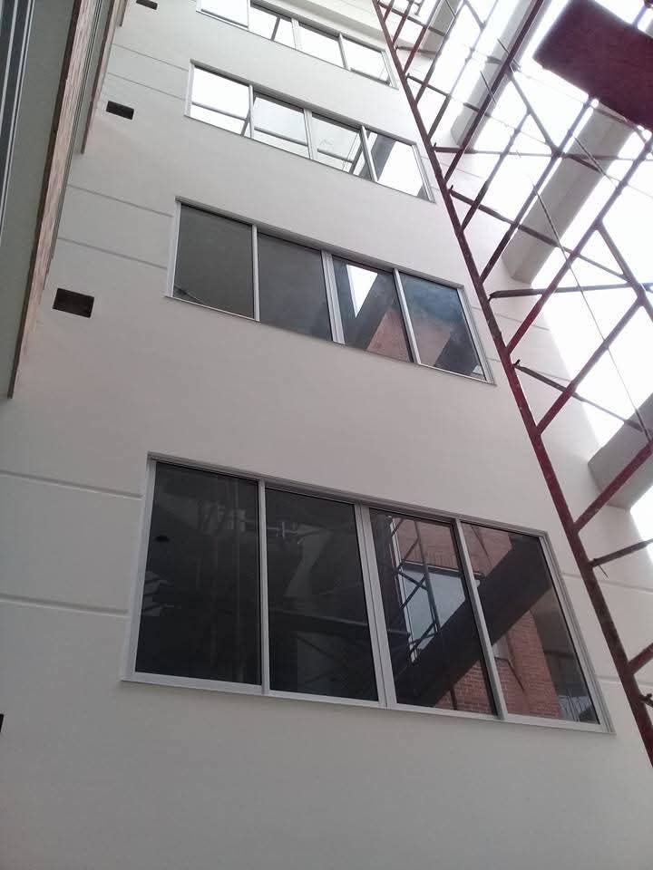 Fachada moderna de un edificio de oficinas de cristal con ventanas reflectantes y cielo azul.