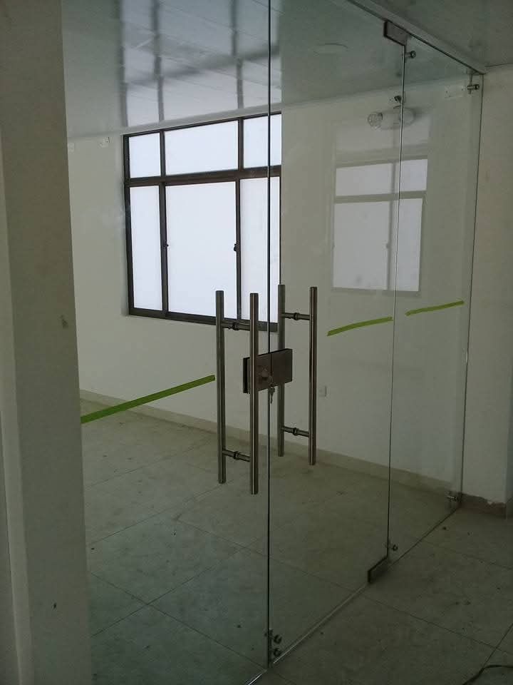 Puertas dobles de cristal enmarcadas en madera oscura que dan acceso al vestíbulo de un edificio moderno con suelo de mármol.