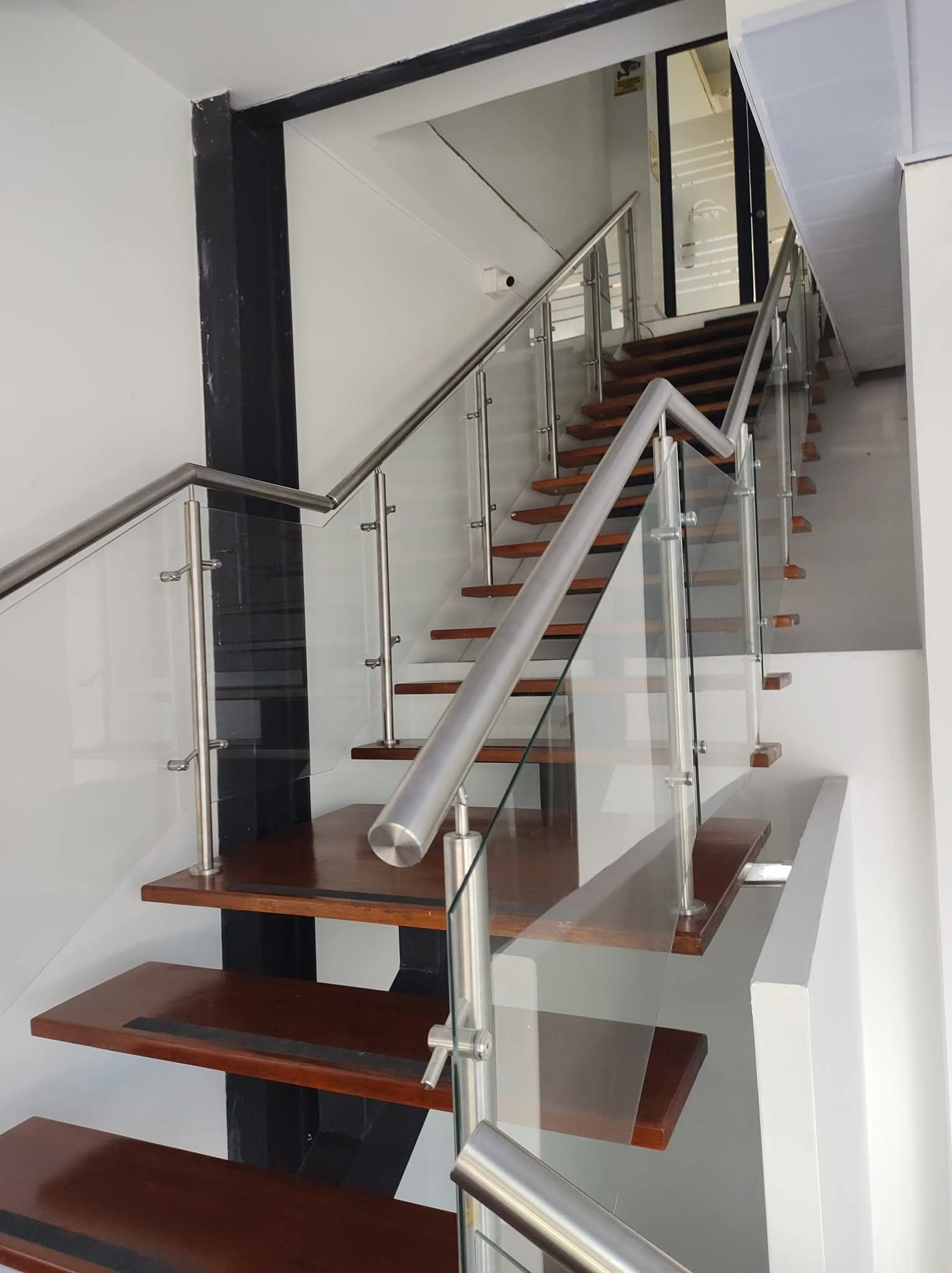 Escalera interior moderna con barandilla de cristal, escalones de madera y paredes blancas.