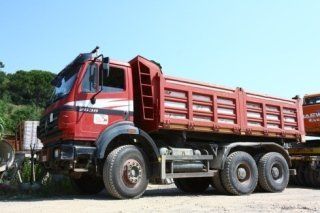 Un camion con cassone ribaltabile rosso è parcheggiato su una strada sterrata.
