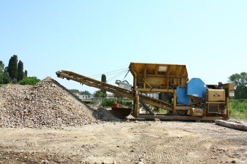 Una macchina è parcheggiata in un campo sterrato accanto a un mucchio di pietre.