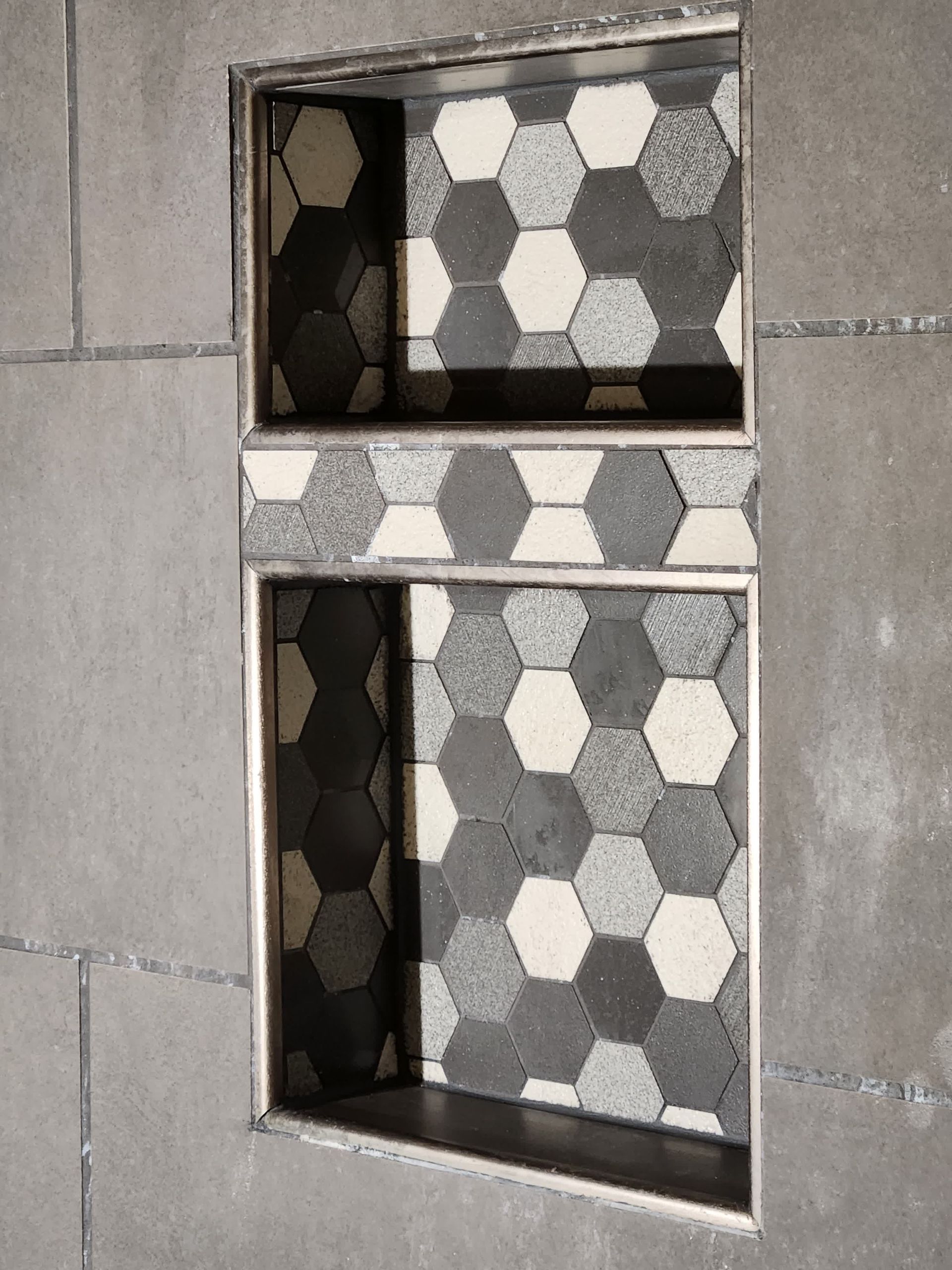 A shower niche with hexagon tiles and a stainless steel frame