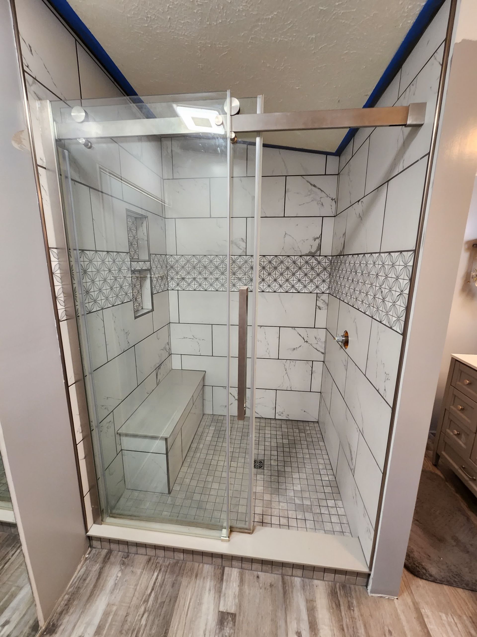 A bathroom with a sliding glass shower door and a bench