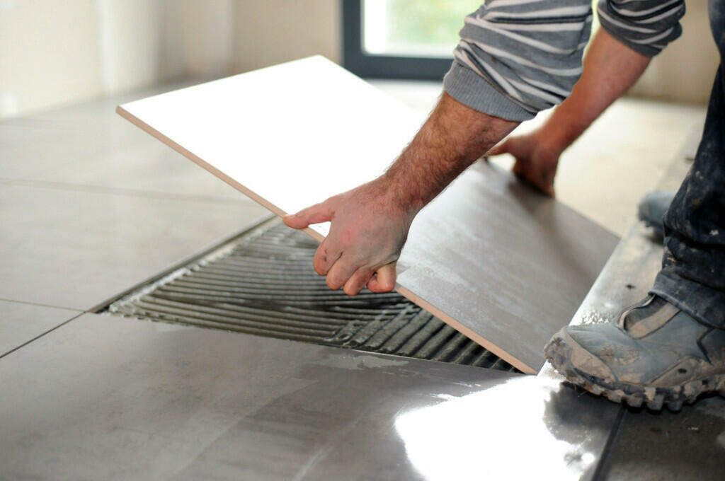 A man is laying a tile on the floor.