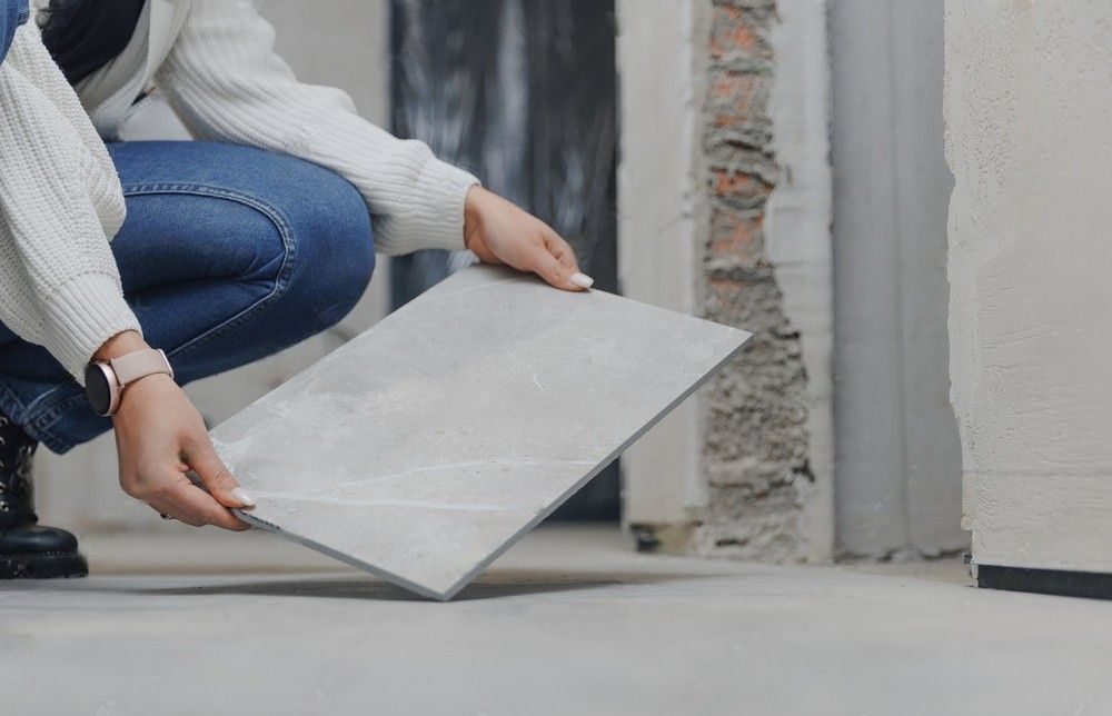 A woman is kneeling down and holding a tile in her hands.