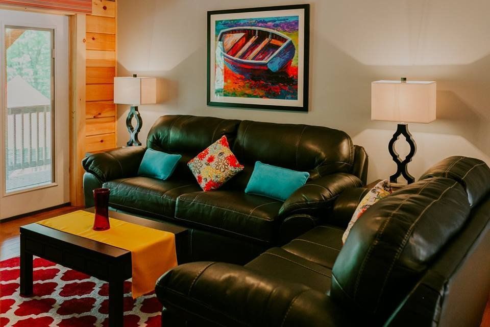 Living room with dark leather furniture, colorful painting, red patterned rug, and lamps.