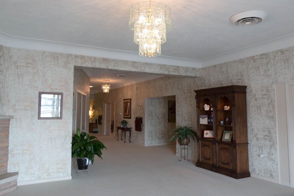 Spacious room with a chandelier, hallway, and a dark wooden cabinet against a textured wall.