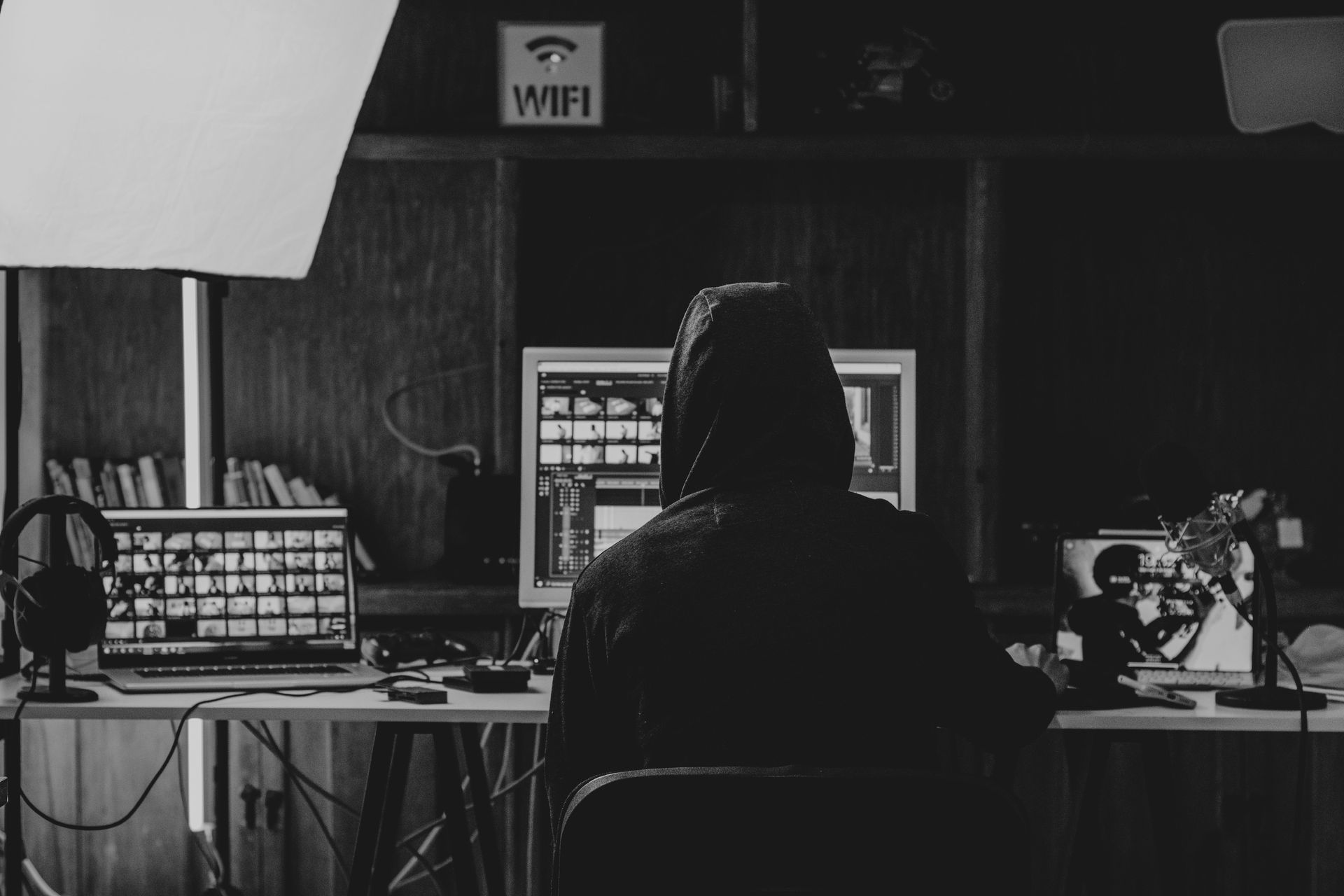 Person at a desk with multiple computer monitors in a dimly lit room, viewed from behind.