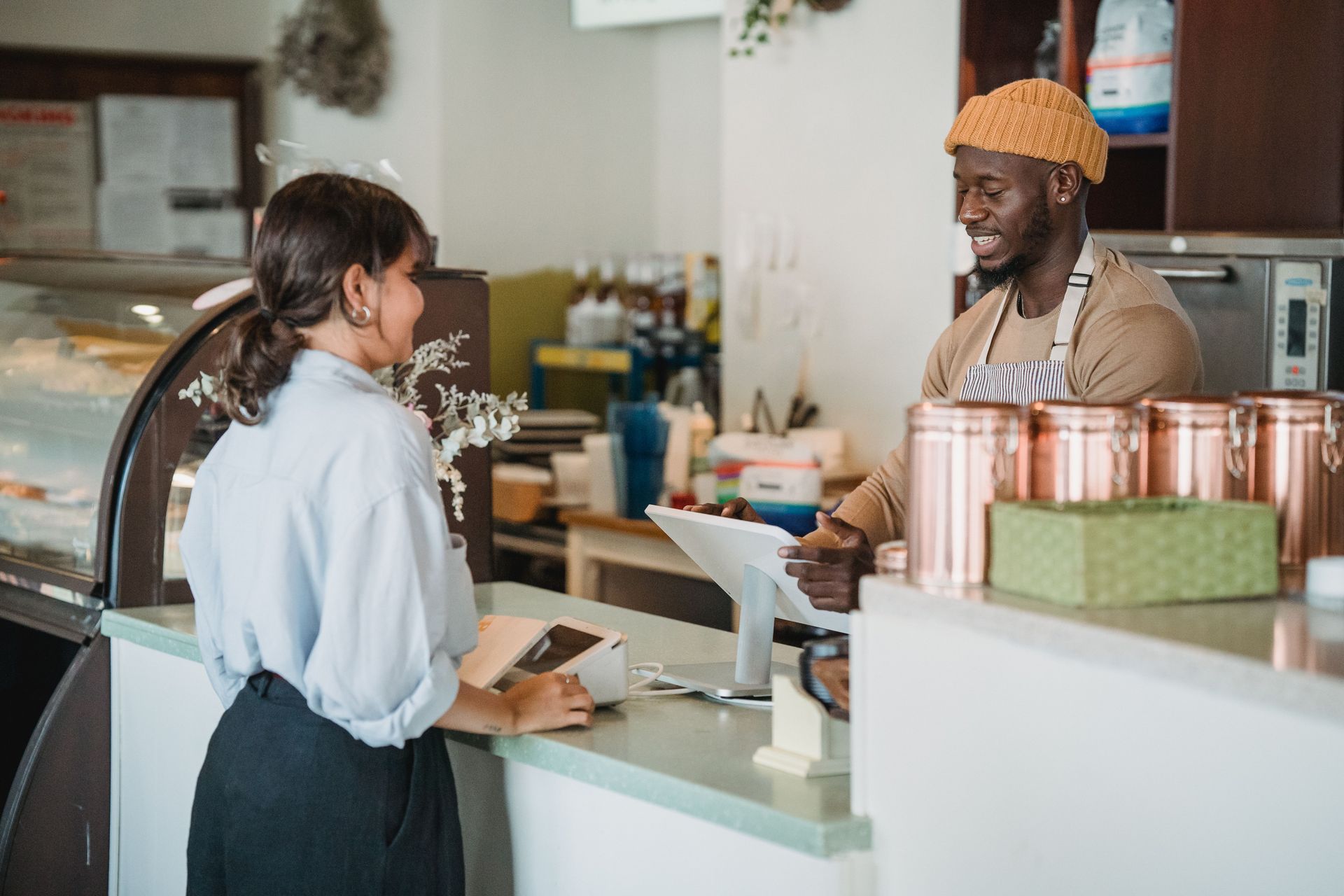 Customer speaking with a barista across a café counter with coffee cups and display items nearby