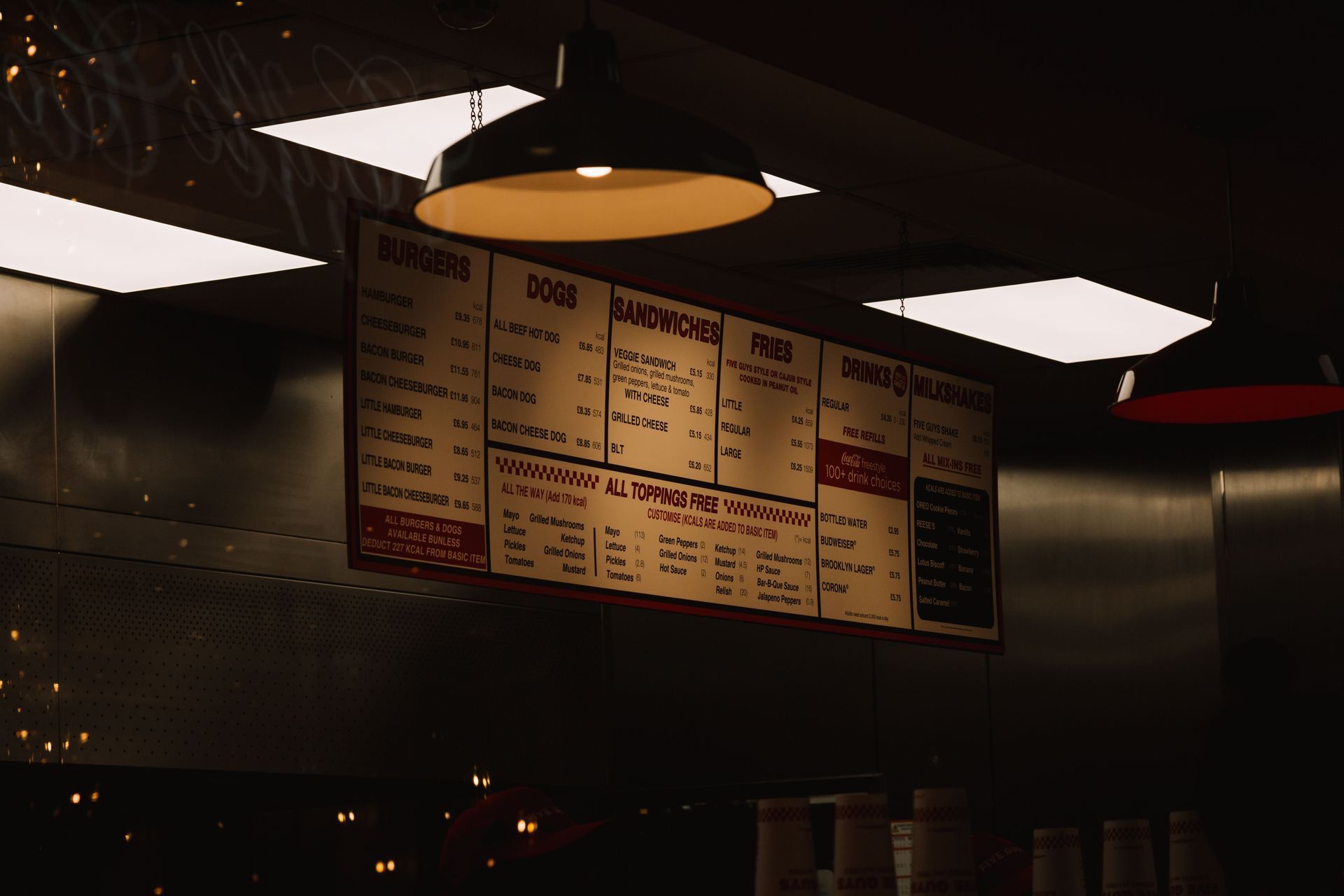 Dimly lit restaurant menu board hanging under ceiling lights in a fast-food counter area