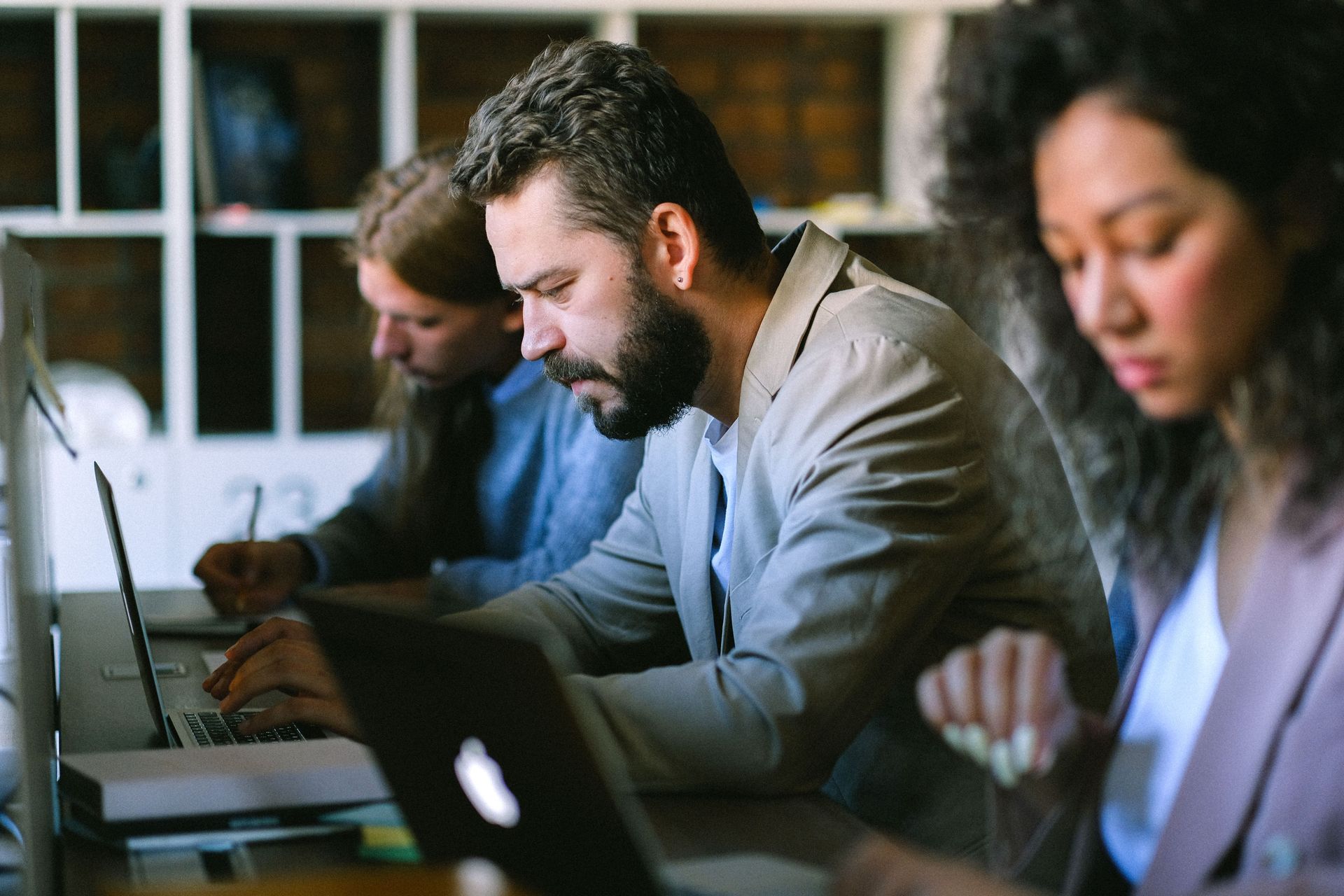 People working on laptops at a desk in a bright office, focused on their screens