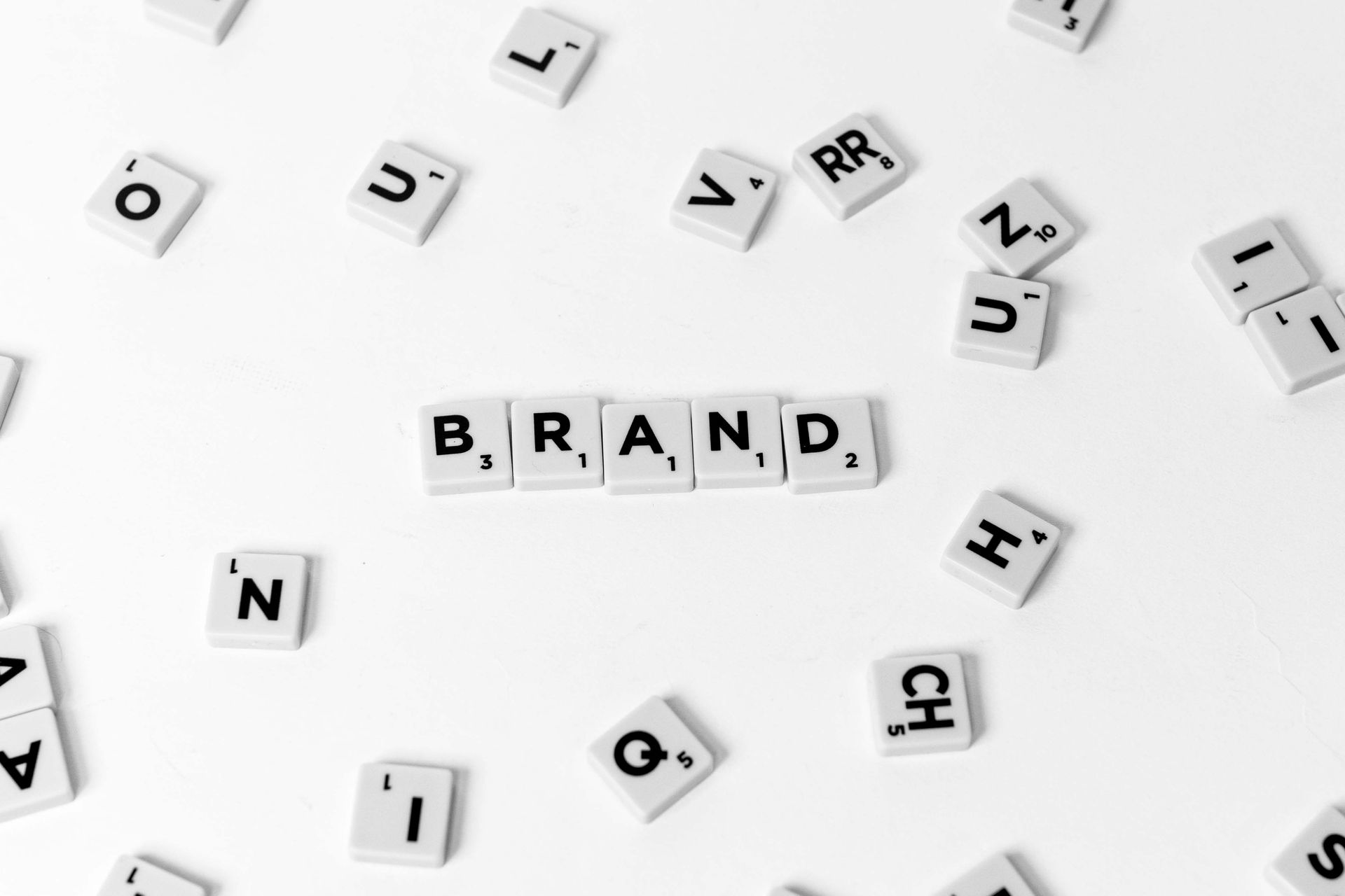 Scrabble tiles spelling “BRAND” on a white background, surrounded by scattered letter tiles