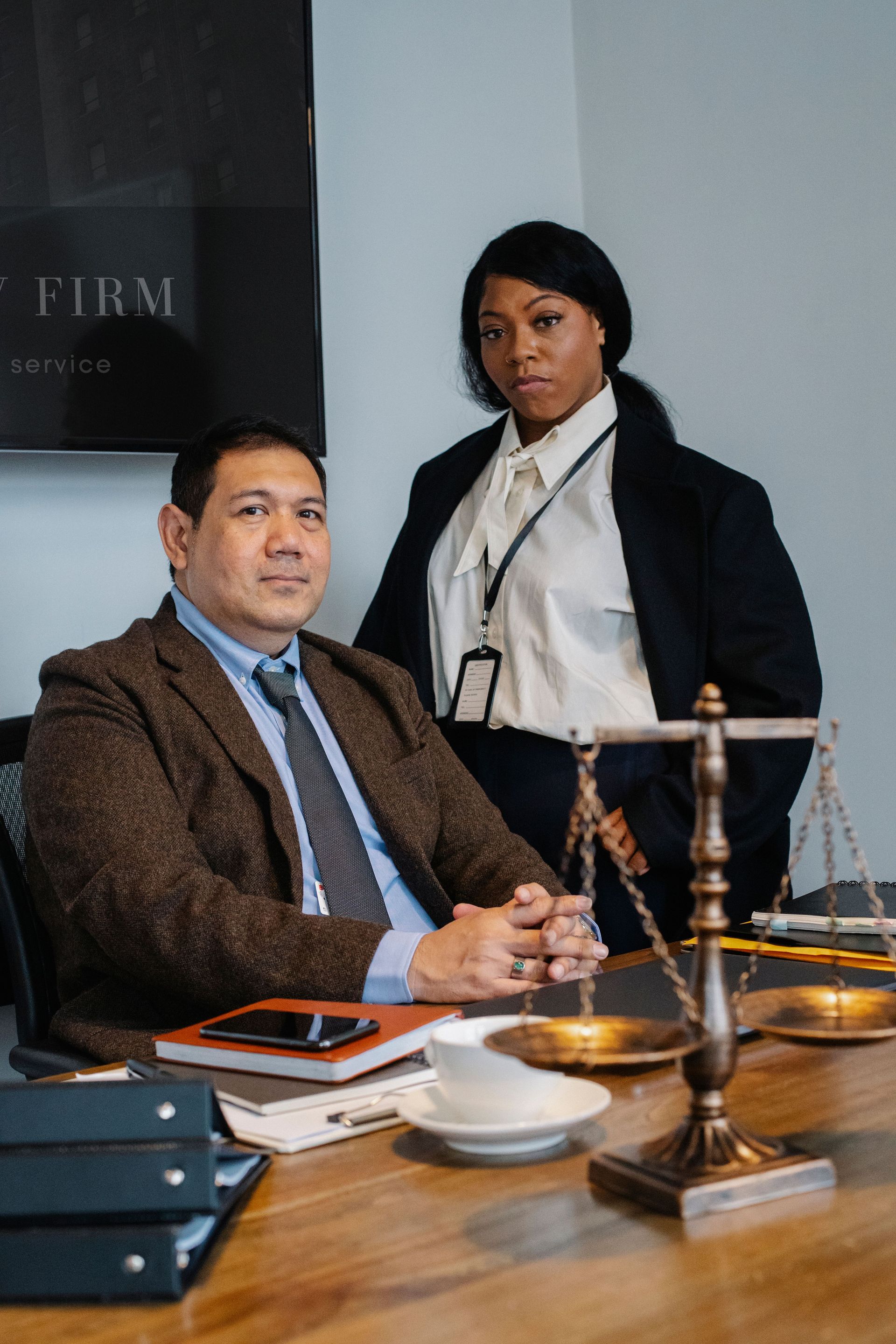 Two businesspeople in an office, seated at a desk with documents and a brass scale.