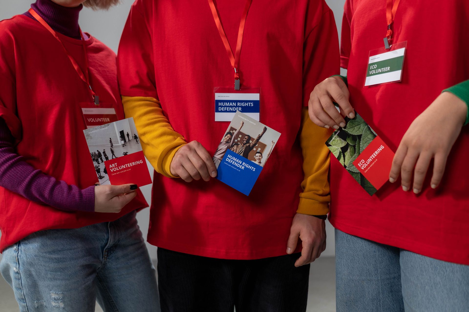 Four people in red shirts hold ID badges and event passes indoors.