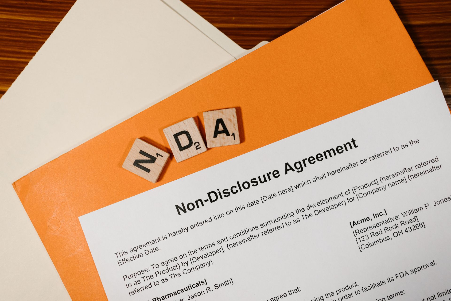 NDA document on an orange folder with letter tiles on a desk