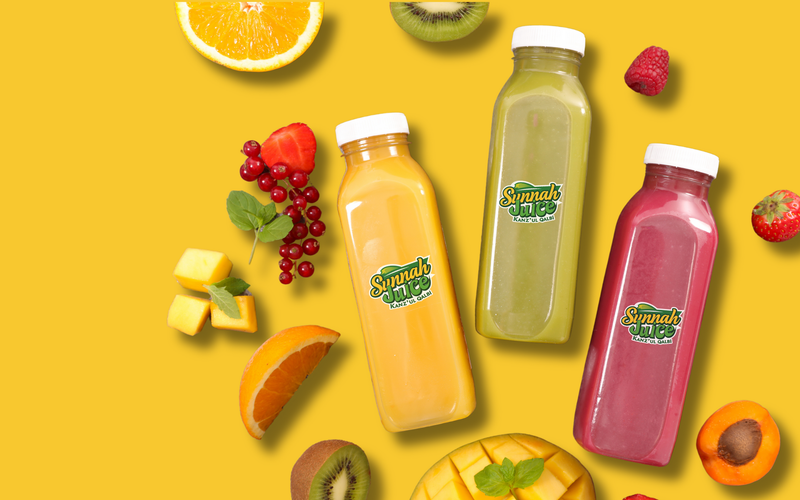 Three Sunnah Juice bottles among fresh fruit on a yellow background