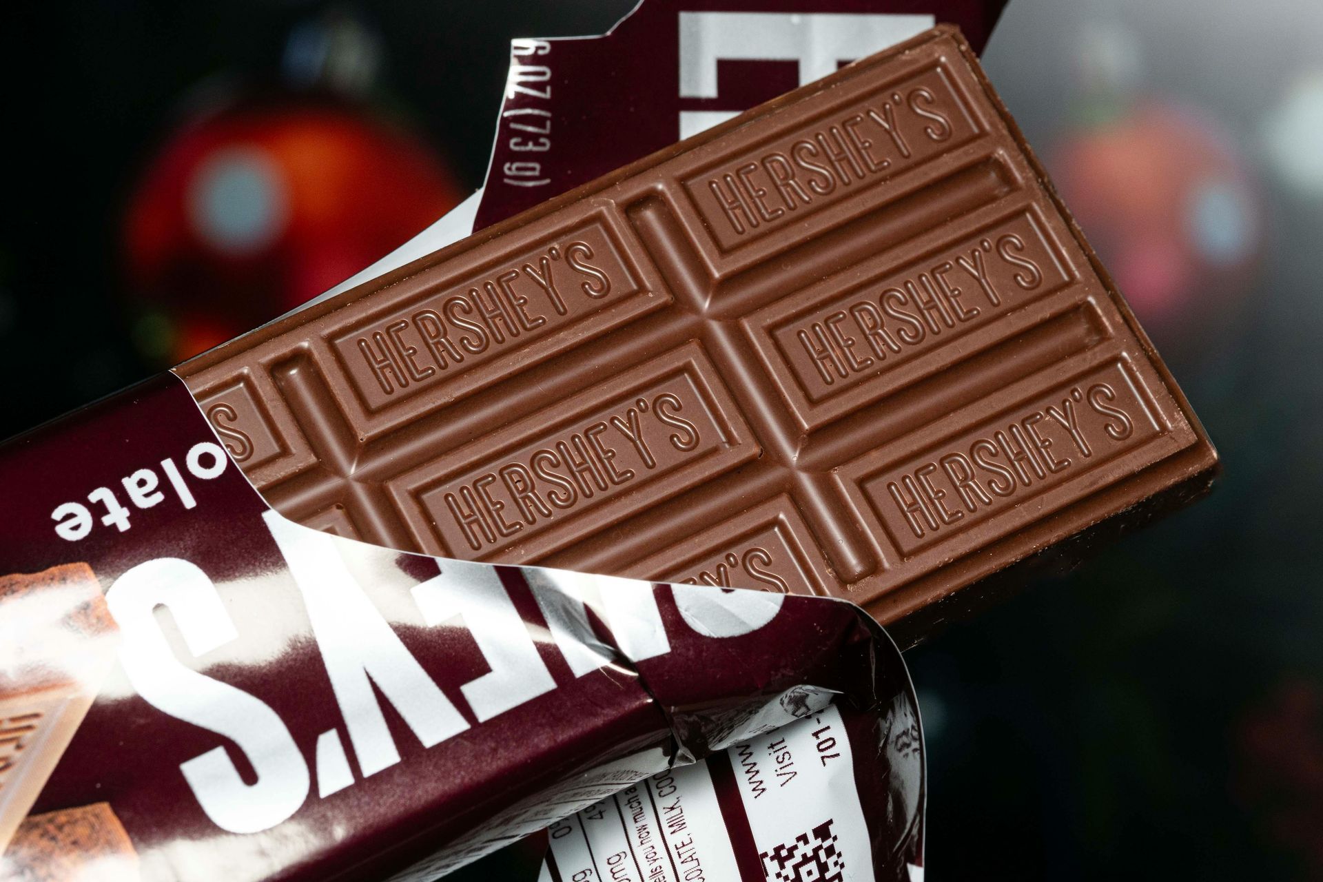 Hershey's chocolate bar partially unwrapped, showing a segmented milk chocolate bar. Dark brown and white packaging.