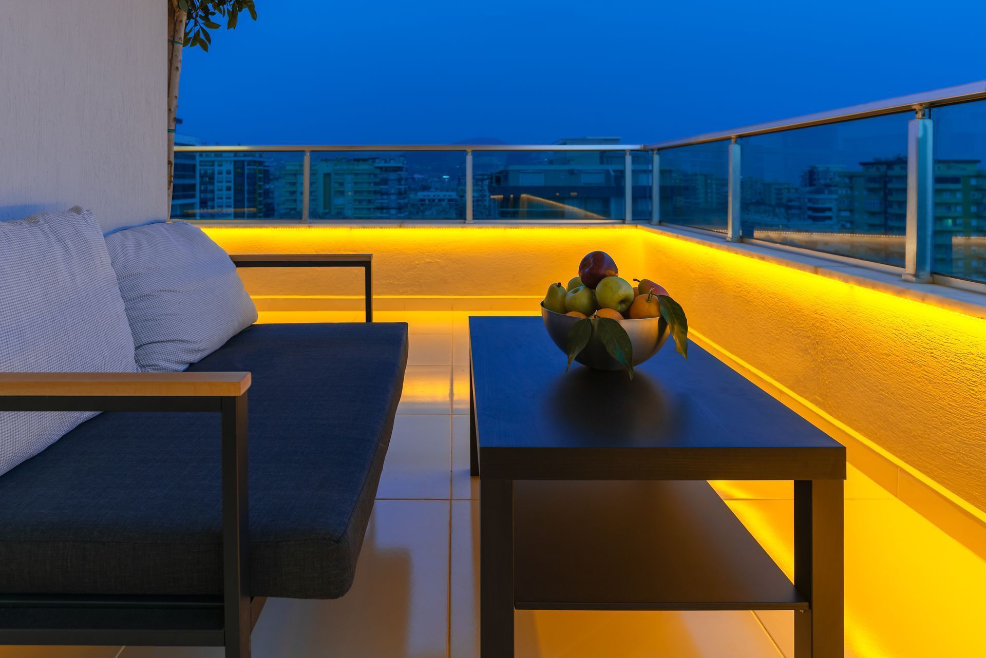 A balcony with a couch and a table with a bowl of fruit on it.
