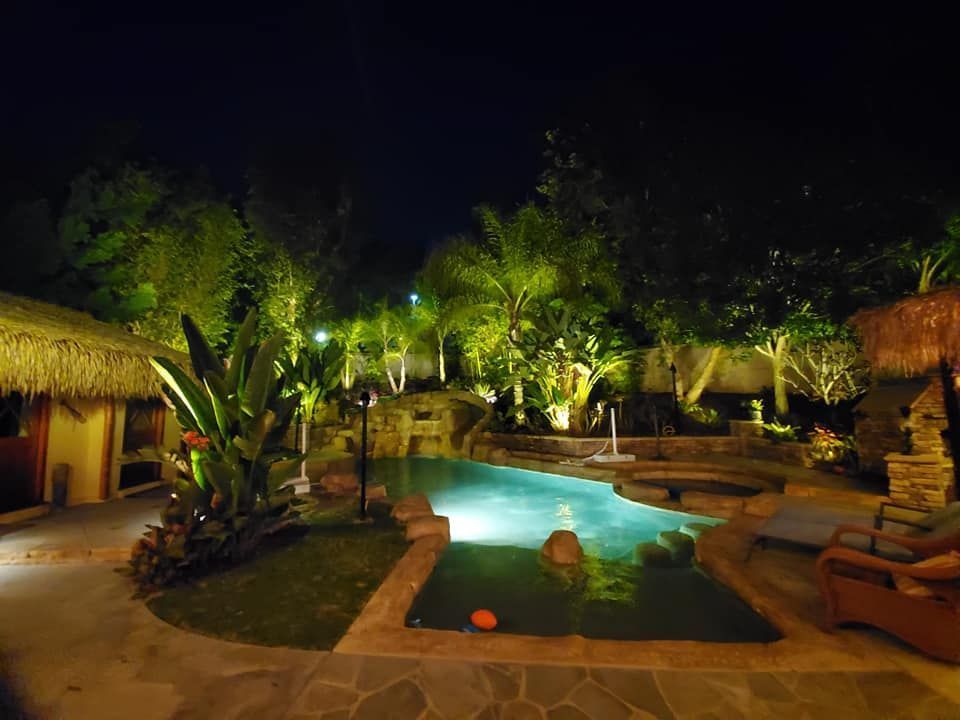 A large swimming pool is lit up at night in a backyard.