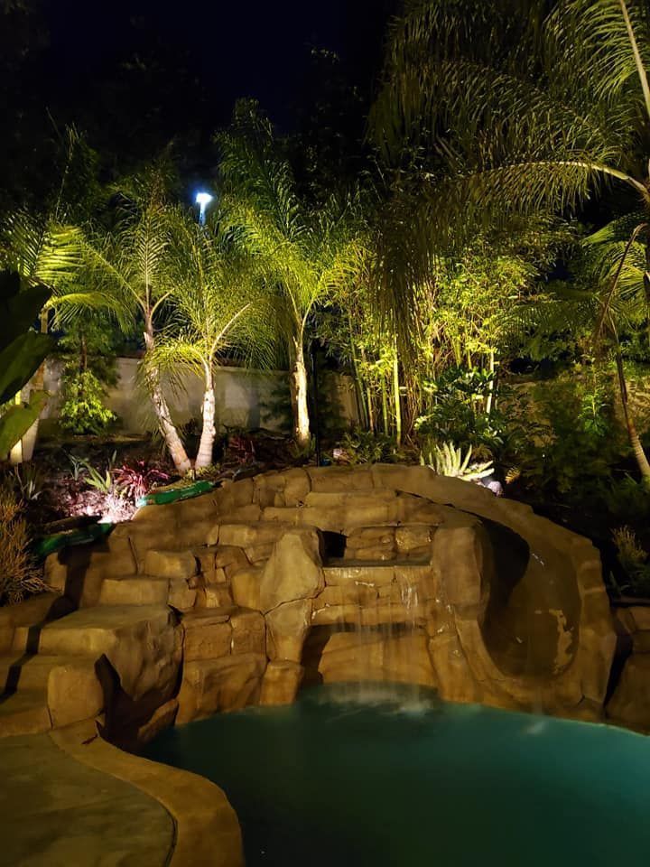 A swimming pool with a waterfall in the backyard at night.