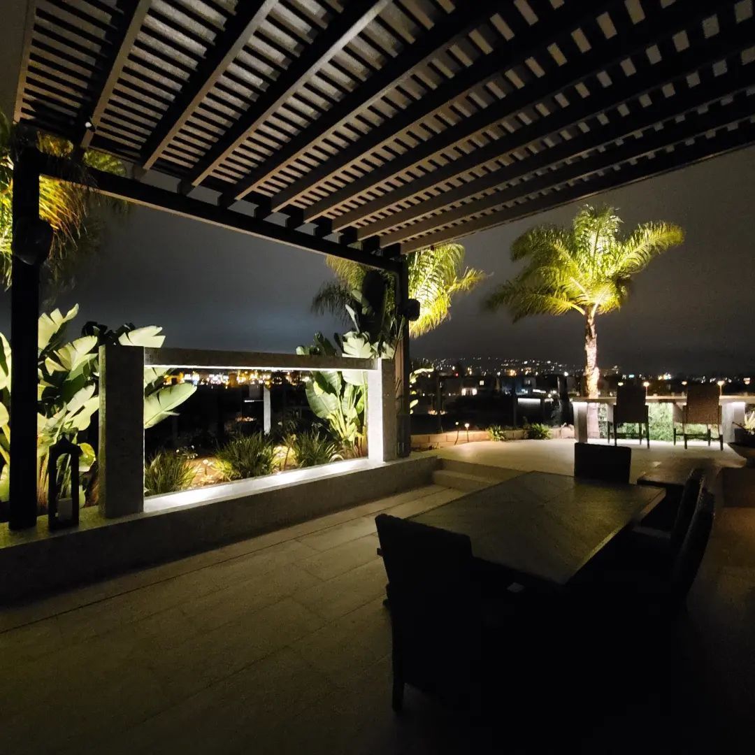 A patio with a table and chairs under a pergola at night