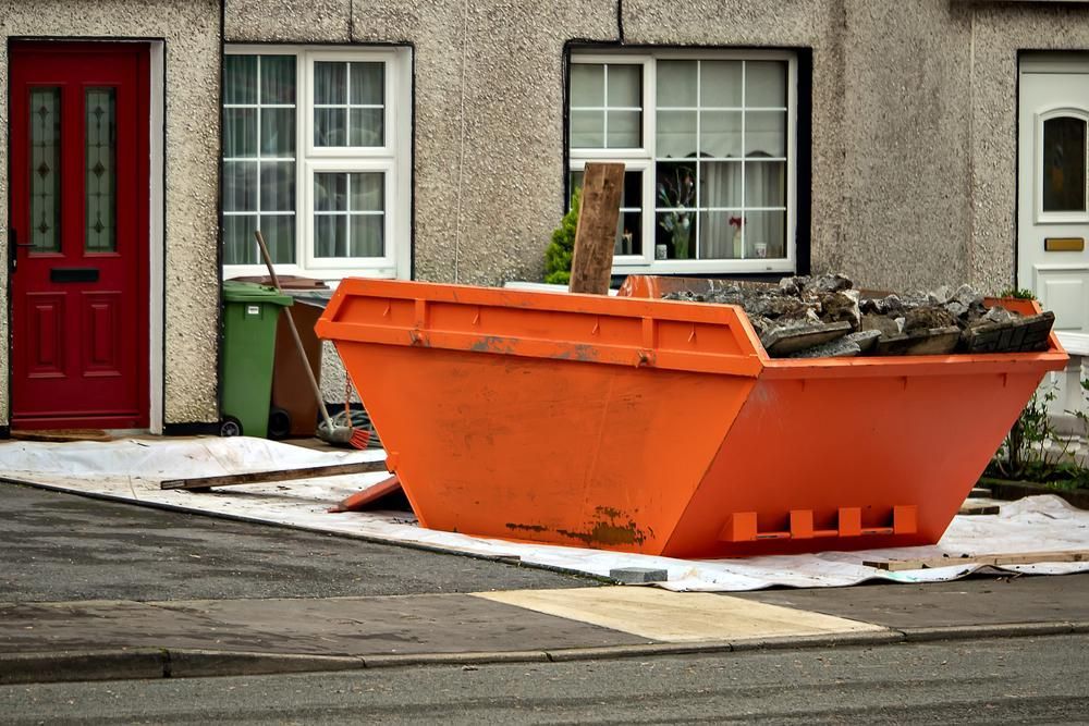 A Large Orange Dumpster is Sitting in Front of a House — I.B.S Skip Bins in Mapleton, QLD