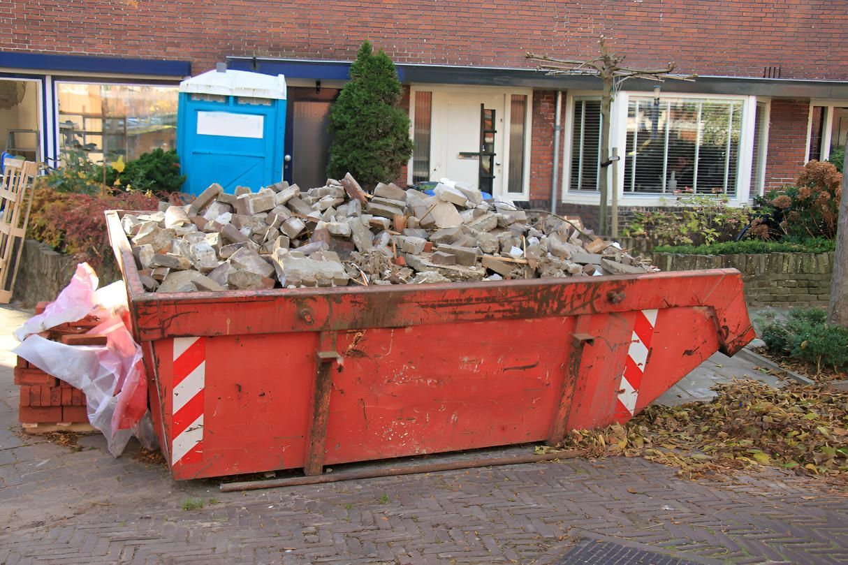 A Red Dumpster Filled With Bricks is in Front of a House — I.B.S Skip Bins in Landsborough, QLD
