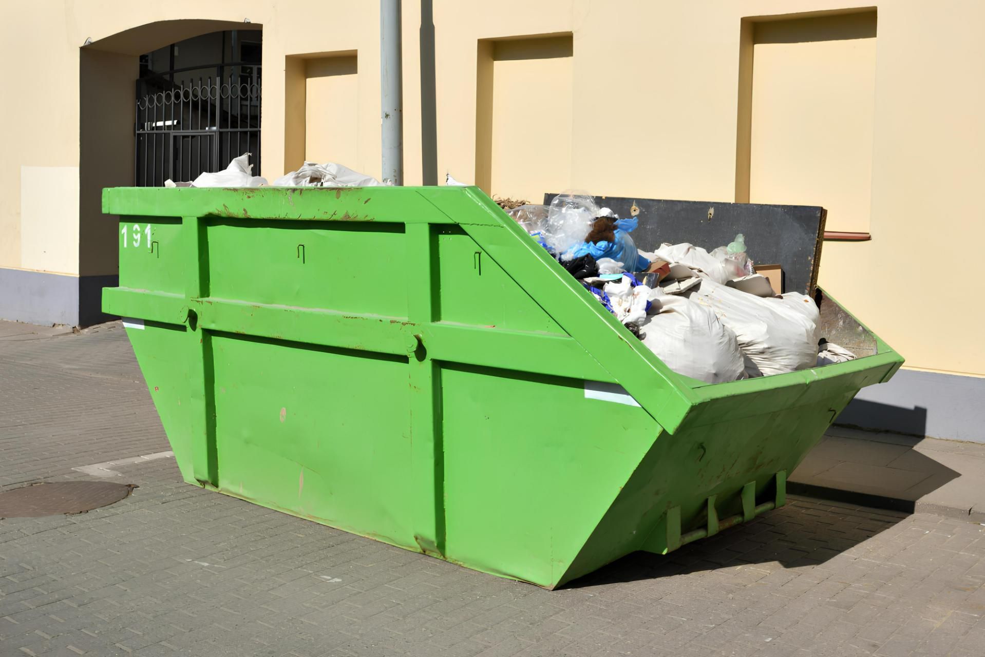 A Green Dumpster Filled With Trash is Parked in Front of a Building — I.B.S Skip Bins in Mapleton, QLD