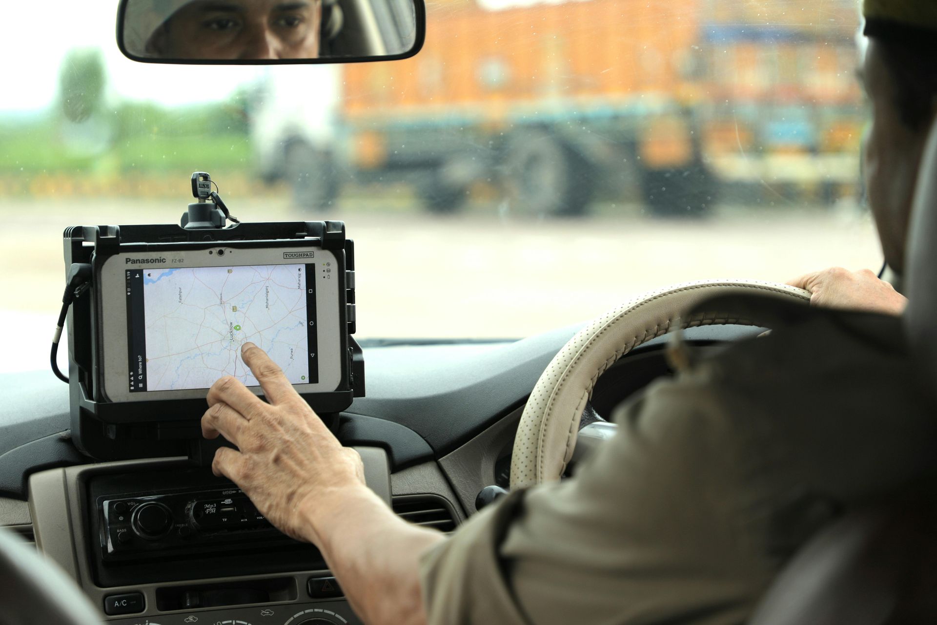 A man is driving a car with a tablet on the dashboard.