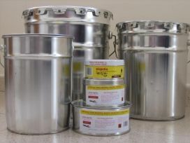 Latas de metal y cubos de pintura apilados sobre una superficie lisa, con un pequeño recipiente etiquetado delante.