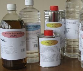 Botellas y latas de aceite de cocina sobre una mesa, con etiquetas blancas y tapones rojos.