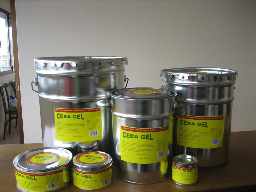Latas metálicas y botes pequeños de Cera Gel sobre una mesa en el interior, con las etiquetas amarillas visibles.