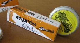 Una lata y una caja de tabaco Exps de color naranja y blanco sobre una mesa, con un recipiente de tapa amarilla cerca.