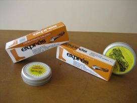 Cajas de productos de color naranja y blanco con dos latas redondas pequeñas sobre una mesa de madera.