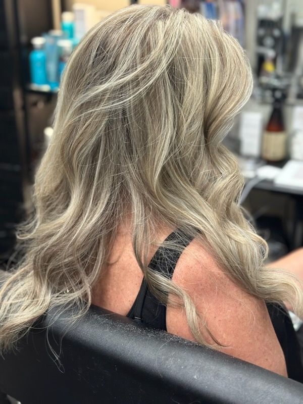 Wavy silver-blonde hair styled in loose layers, seen from behind in a salon chair
