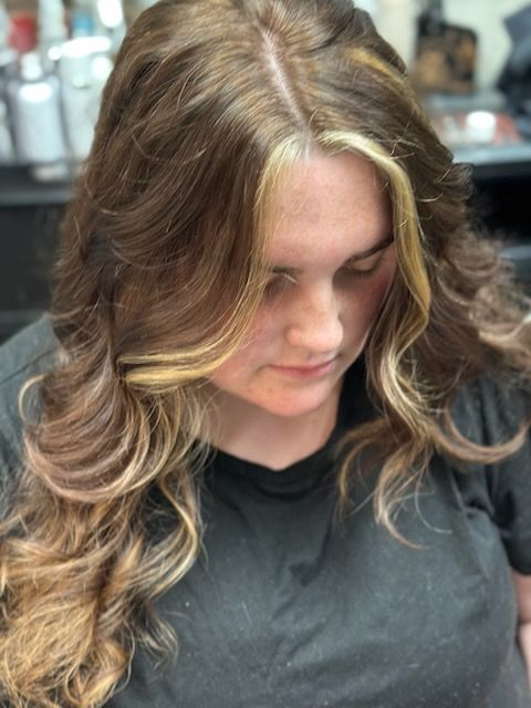 Person with wavy blonde hair looking down, wearing a black shirt in a salon setting