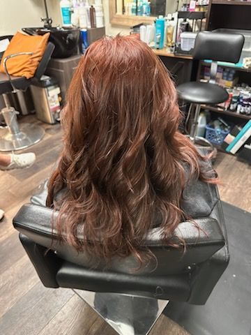 Long wavy auburn hair styled in a salon chair, with tools and supplies visible around it.