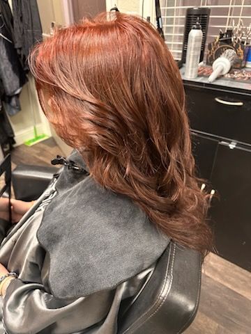 Side view of a salon client with layered auburn hair in a styling chair