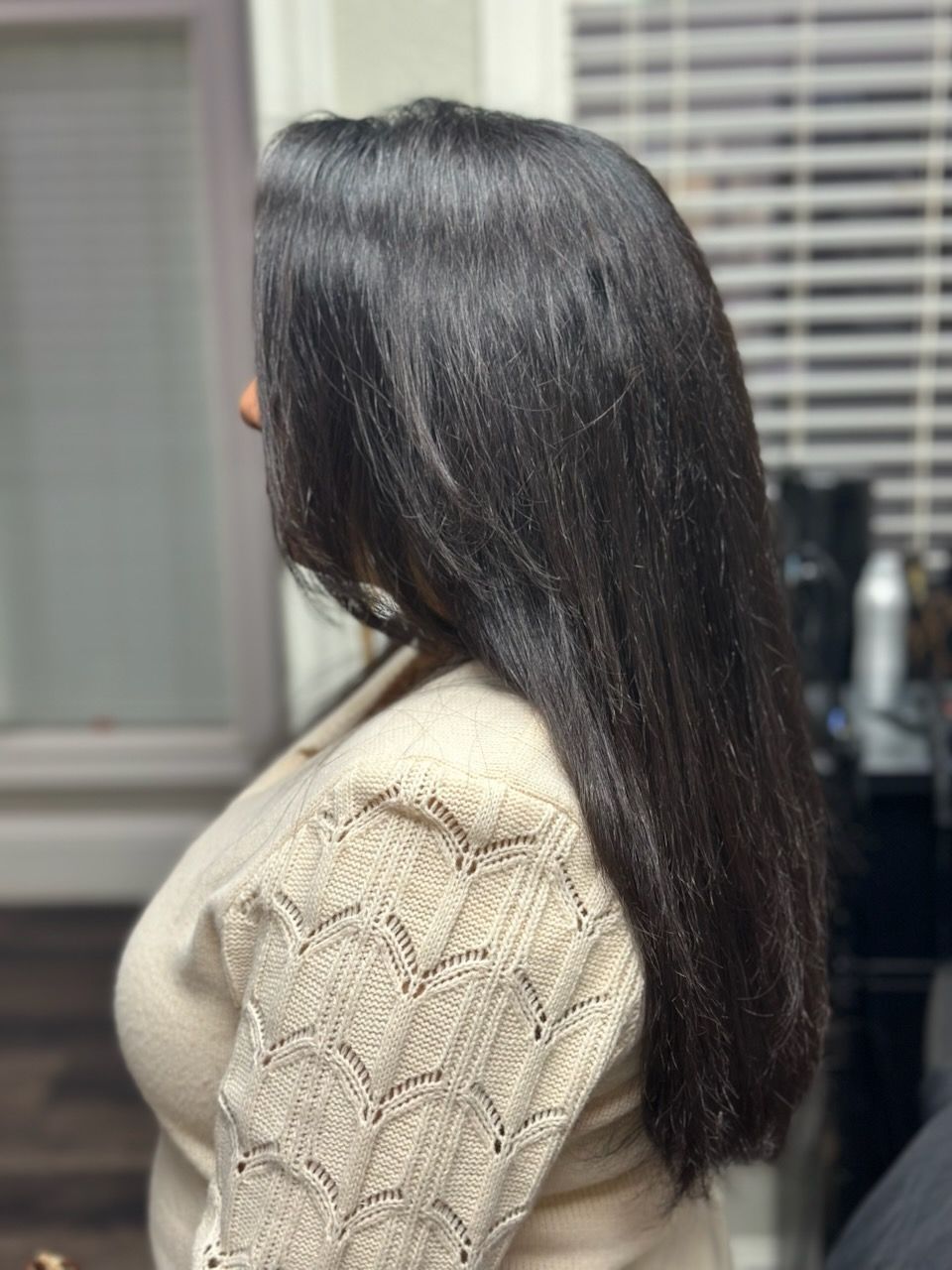 Woman with long dark hair in a beige sweater, shown in side profile indoors.
