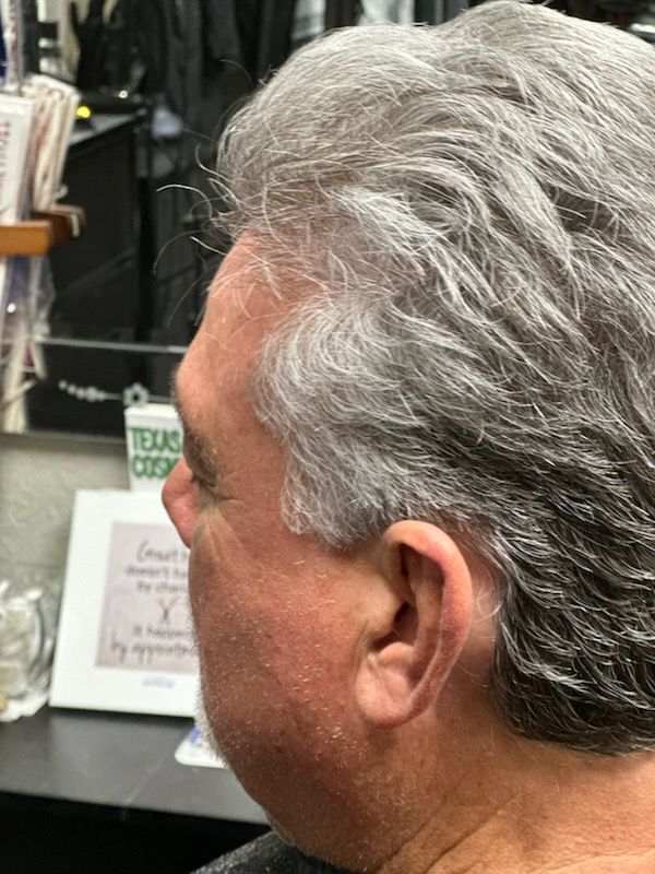 Profile of a man with gray hair in a barber shop, facing left near a counter
