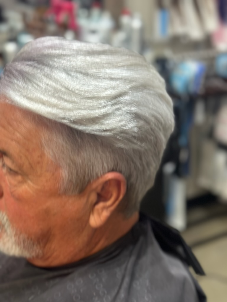 Man with short silver hair in profile, seated indoors against a blurred background.