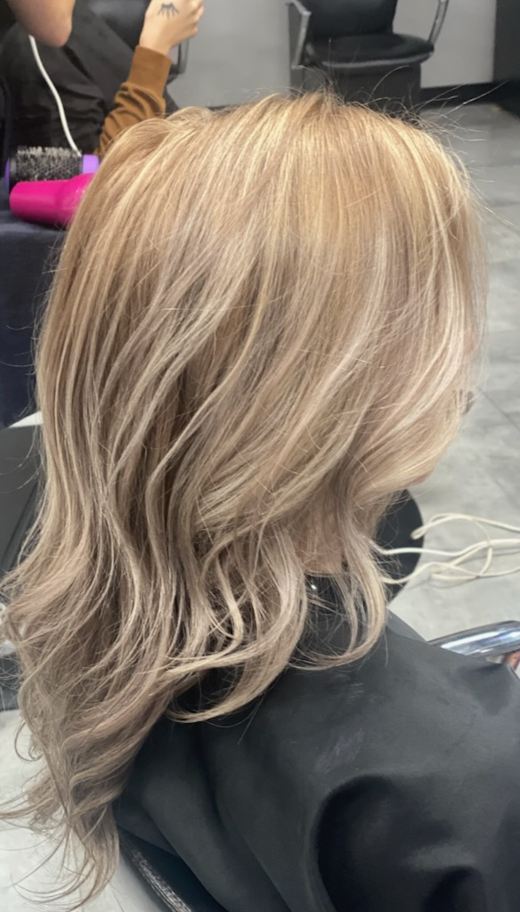 Wavy shoulder-length blonde balayage hairstyle in a salon chair, viewed from behind.