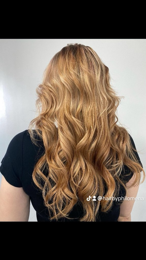 Long wavy blonde hair with curled ends against a light gray background